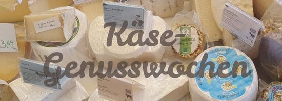 Auswahl verschiedener Käsesorten, die auf einem Tisch ausgestellt sind. Im Vordergrund steht der Text "Käse-Genusswochen".